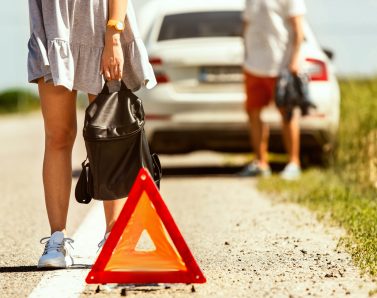 The young couple broke down the car while traveling on the way to rest. They are trying to stop other drivers and ask for help or hitchhike. Relationship, troubles on the road, vacation.